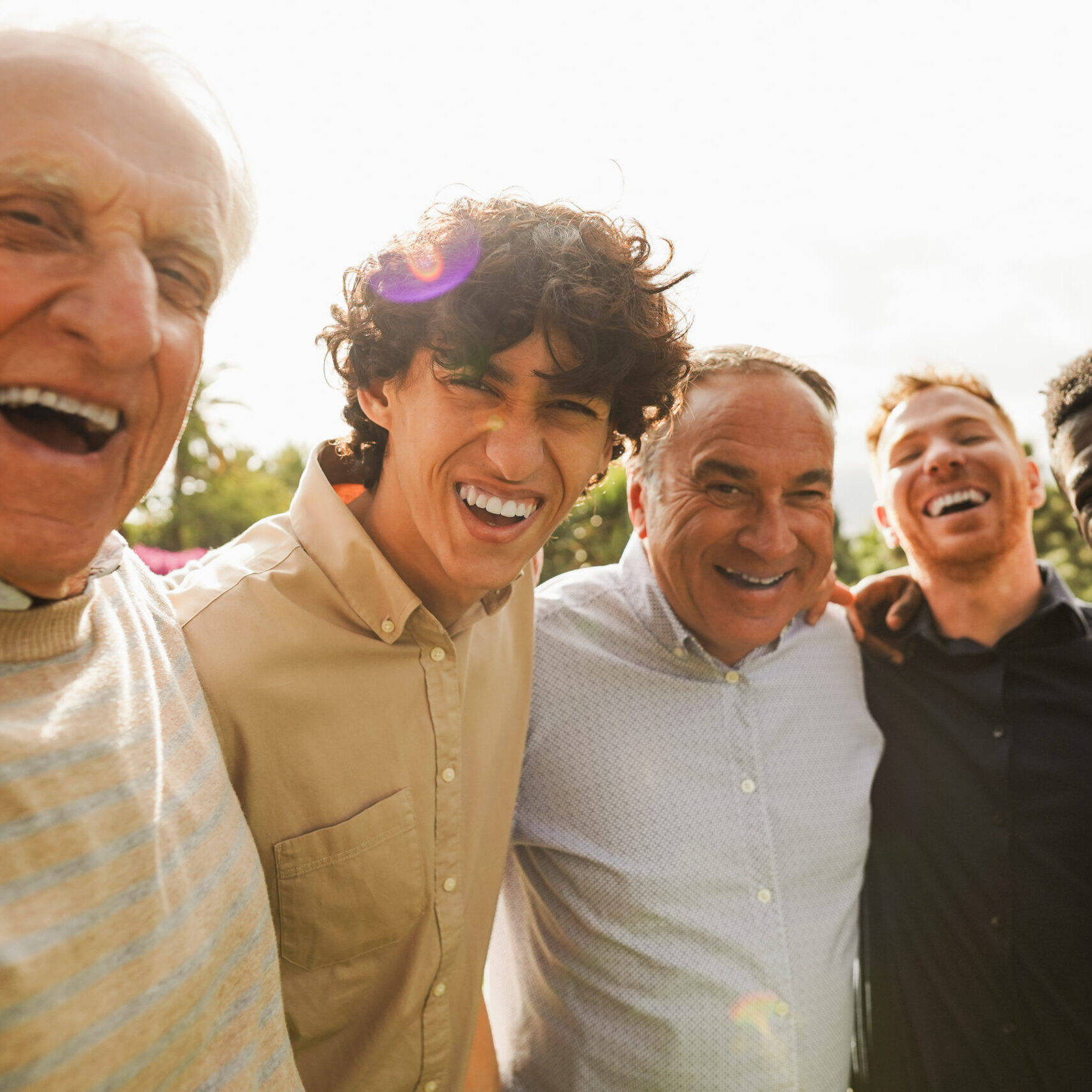 Multi generational men smiling in front of camera - Male multiracial group having fun togheter outdoor - Focus on left boy face